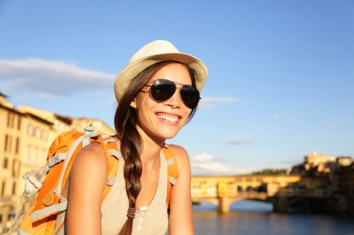 Backpacking women traveler on travel in Florence wearing sunglasses smiling happy by Ponte Vecchio during vacation holidays in Tuscany, Italy, Europe.